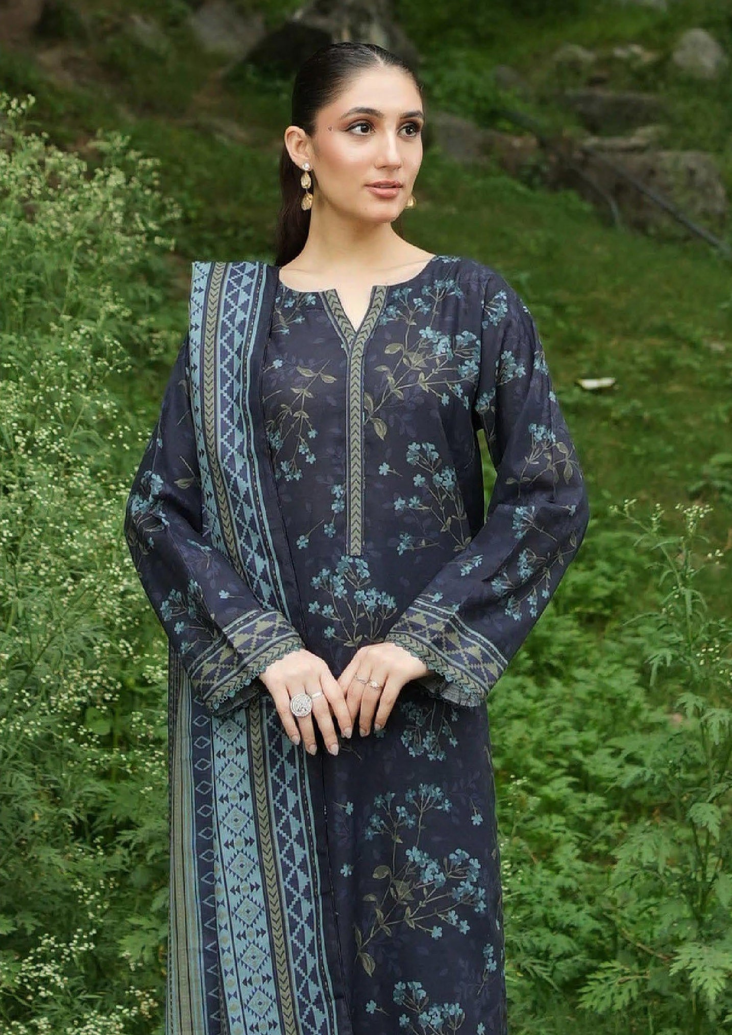 Woman wearing a dark blue traditional outfit with floral patterns in a natural setting.